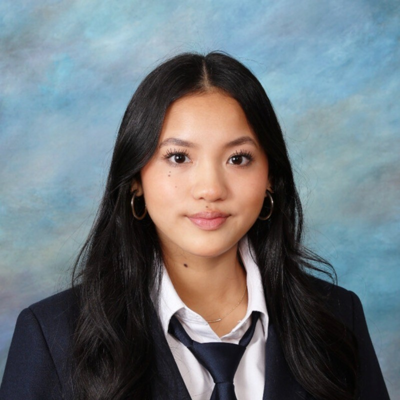 Professional headshot of Leah Tran in a navy blazer, white shirt, and tie; square studio portrait.